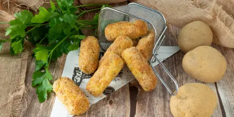 Crocchette di patate in friggitrice ad aria, dorate e croccanti, pronte per essere gustate. Accanto, patate fresche e prezzemolo.