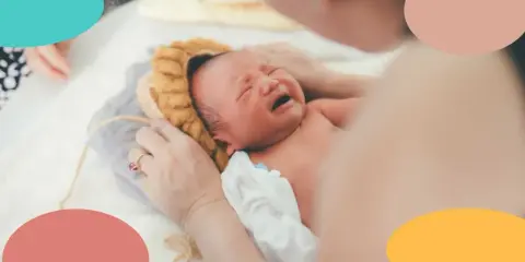 Un recién nacido no duerme, llora desconsoladamente mientras una mano le acaricia la cabeza.