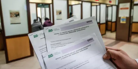 Dłoń trzyma formularze ZUS dotyczące wniosku o rodzicielskie świadczenie uzupełniające. To krok do ponownego przeliczenia emerytury ze względu na długość życia.