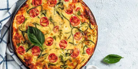 Torta salata vegana con zucchine e pomodorini, guarnita con basilico fresco.