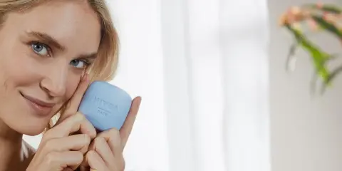 Une femme blonde tient un pain de savon bleu Nivea Face. Elle sourit, sa peau semble douce. Ce savon a un pH neutre, combien est-il doux pour votre visage ?