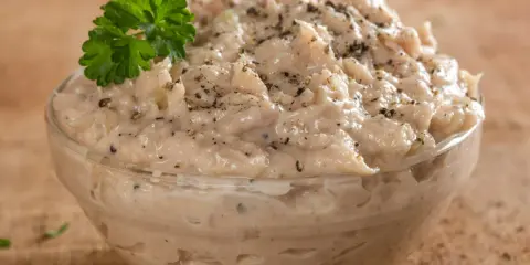 Pyszna pasta z tuńczyka w szklanej miseczce, doprawiona pieprzem i udekorowana gałązką natki pietruszki. Idealna na kanapki.