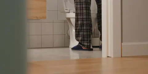 Osoba w piżamie stoi przy toalecie, widać jej nogi i kapcie. Czyżby pojawiły się bąbelki w moczu?