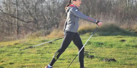 Kobieta w stroju sportowym ćwiczy nordic walking, używając kijków. Widać, jakie kije do nordic walking są lekkie i wygodne.