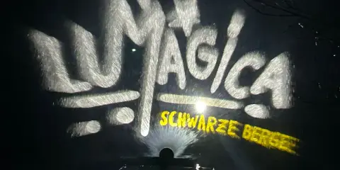LUMAGICA Schwarze Berge Schriftzug auf Wasserprojektion bei Nacht.