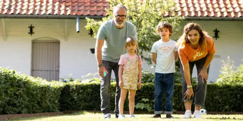 Une famille s'amuse dans le jardin avec un jeu de pétanque en ligne. Les boules colorées sont alignées sur l'herbe.