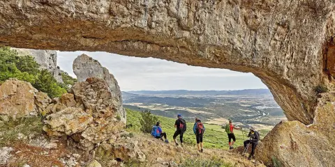 Senderismo Navarra: grupo de excursionistas admira un paisaje montañoso desde debajo de un arco de roca natural.