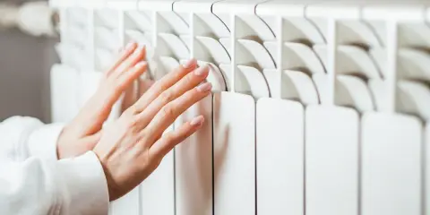 Manos cálidas sobre un convector blanco, sintiendo el calor del invierno.