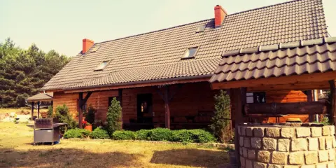 Drewniany dom pod kasztanem, z kamienną studnią i grillem, otoczony zielenią i lasem.
