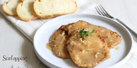 Tre scaloppine al vino bianco su un piatto bianco, guarnite con timo fresco, accompagnate da fette di pane tostato.