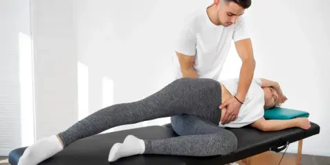 Fizjoterapeuta wykonuje terapię manualną, pomagając pacjentce w rozluźnieniu biodra. To właśnie terapia manualna co to jest – technika leczenia bólu i dysfunkcji.