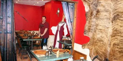 Un homme se tient dans un restaurant moyen âge décoré d'une peau d'ours et d'une épée.
