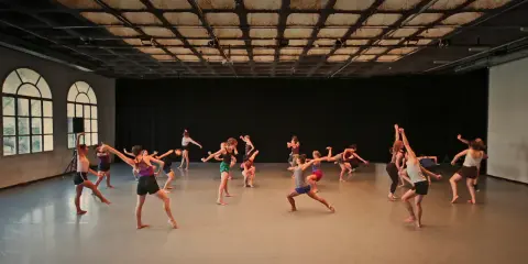 Grupa tancerzy wykonuje dynamiczny gaga taniec w przestronnej sali.