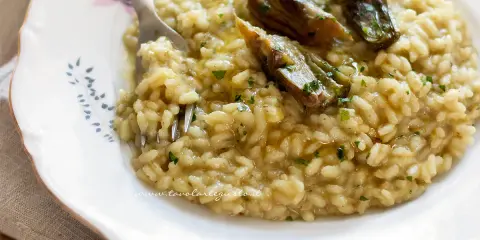 Un cremoso risotto con carciofi freschi, guarnito con prezzemolo tritato e un filo d'olio.