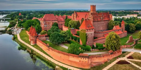 Potężny zamek w Malborku, jedna z największych atrakcji Polski, otoczony murami obronnymi i rzeką Nogat.