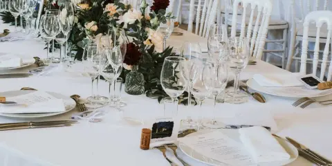 Un élégant dressage d'une table à la française, prêt pour un festin. Verrerie étincelante, fleurs fraîches et menus attendent les convives.