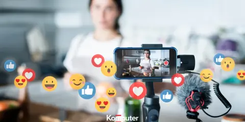Kobieta nagrywa filmik w kuchni, a wokół telefonu unoszą się emotikony. Idealne do aplikacji do oglądania filmów i tworzenia treści.