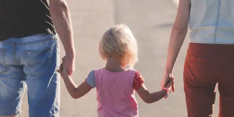 Rodzina idzie razem, trzymając się za ręce. Dziecko z blond włosami, w kolorowej bluzce, między rodzicami. Może to być obraz rodziny, która radzi sobie z zaburzeniami zachowania ICD 10.