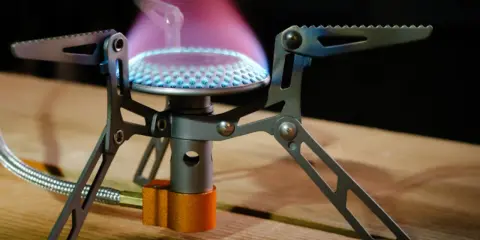 Estufa portátil sin electricidad ni gas, con llama azul y púrpura, ideal para acampar.