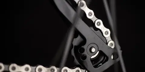 Jak dobrać łańcuch do roweru? Detal przerzutki tylnej z metalowym łańcuchem rowerowym na czarnym tle.