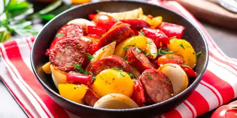 Salsiccia e patate in padella, un piatto saporito con peperoni rossi e gialli, cipolle e erbe aromatiche fresche.