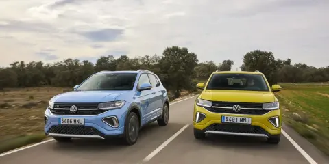 Un Volkswagen T-Cross azul y un T-Roc amarillo circulan por una carretera rural.