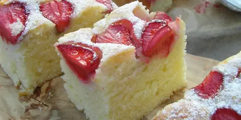 Puszyste ciasto na maślance z kawałkami truskawek, posypane cukrem pudrem. Idealne na letnie popołudnie.