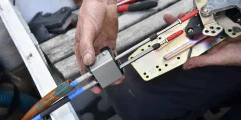 Main d'un mécanicien démontant le boîtier de commande d'un bateau, révélant les câbles et le mécanisme.