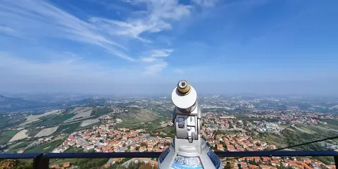 Telescopio con vista panoramica su cosa vedere a San Marino. Il paesaggio collinare e la città si estendono sotto un cielo azzurro con nuvole sottili.