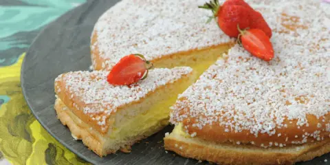 Un délicieux gâteau génoise crème pâtissière, saupoudré de sucre et garni de fraises fraîches.