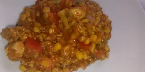 Pyszne kaszotto z kurczakiem, kukurydzą i pomidorami na białym talerzu.