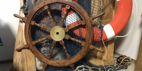 Roue de gouvernail en bois, filet de pêche, bouée de sauvetage orange et pagaies évoquent un safran de bateau prêt pour l'aventure.