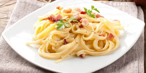 Pyszny makaron carbonara z boczkiem i natką pietruszki na białym talerzu.