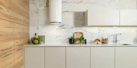 Nowoczesna kuchnia z białym, cylindrycznym okapem. Aranżacje z drewnianymi frontami i marmurową płytką ścienną tworzą elegancką całość.