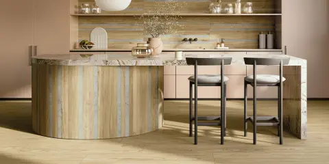Interni di una casa super moderna: isola cucina in legno e marmo, sgabelli grigi, mobili rosa cipria e pavimento in parquet chiaro.
