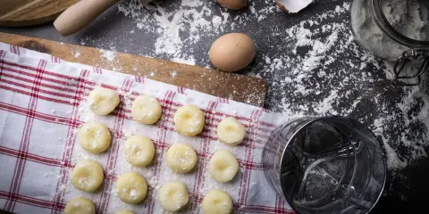 Surowe kluski śląskie ułożone na ręczniku, obok jajka, mąka i wałek.