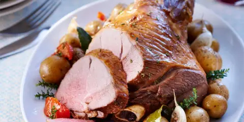 Un gigot d'agneau rôti, tranché, servi avec des pommes de terre nouvelles, tomates et ail. Parfait pour savoir que faire avec des morceaux de gigot d'agneau.