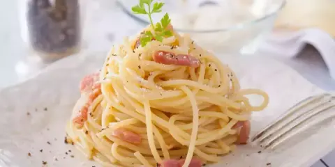 Un plat de tagliatelles carbonara crémeuses, garni de lardons et de persil frais, prêt à être dégusté.