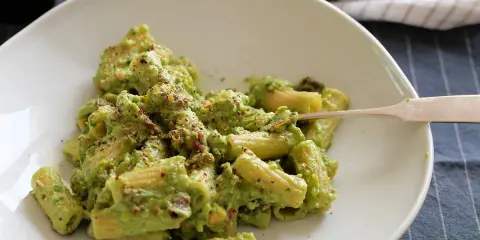 Cremige Avocado-Pasta mit Kräutern und Gewürzen auf einem weißen Teller, bereit zum Genießen.