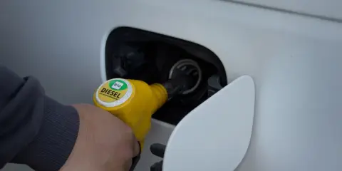 Ręka trzymająca żółtą dyszę dystrybutora, tankuje samochód. Na dyszy widnieje napis "DIESEL B10".