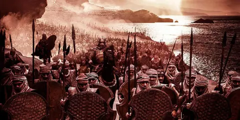 Eine Armee von griechischen Soldaten in der Antike marschiert am Meer entlang. Ein Anführer auf einem Pferd reitet vor ihnen.