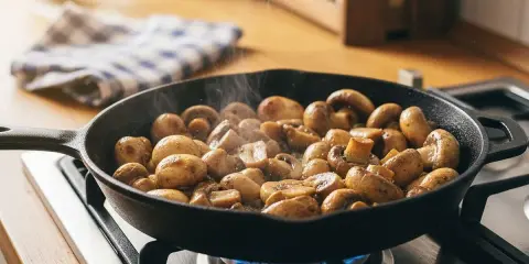 Pilze braten in einer Gusseisenpfanne auf dem Herd. Dampf steigt auf, während die Pilze goldbraun werden.