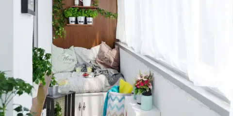 Przytulna loggia w bloku z wygodną kanapą, ziołami na półkach i bukietem kwiatów. Idealne miejsce na relaks.