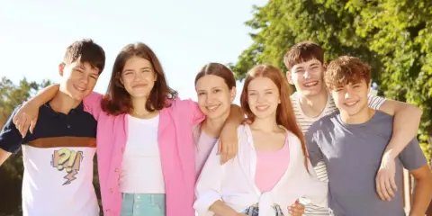 Szczęśliwa grupa nastolatków, uśmiechnięci, objęci, jakby przeżywali pierwsze etapy związku nastolatków.