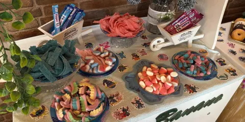 Una mesa llena de todas las chuches del mundo: gominolas azules, rojas, rosas y de muchos colores, dispuestas en cuencos y carretillas.