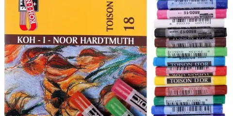 Pudełko z pastelami Koh-i-Noor i stos kolorowych pasteli olejnych.