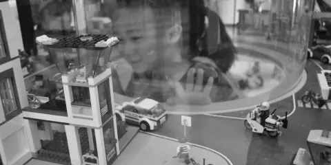 Bambina osserva con stupore un **reportage fotografico** di idee con costruzioni Lego: un commissariato, auto della polizia e personaggi in azione.