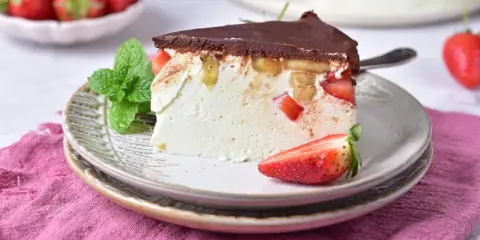 Pyszny keto sernik na zimno z kawałkami truskawek i bananów, polany czekoladą. Idealny deser dla dbających o linię.