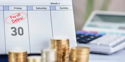 Kalendarz z zaznaczonym "Pay off Debts!" i sterty monet. Długi w ZUS to jak więzienie, ale spłata to wolność.