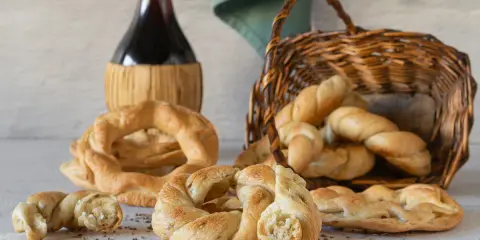 Pane intrecciato e ciambelle, ispirazione per ricette ciociare, accanto a una bottiglia di vino rosso e un cesto di vimini.